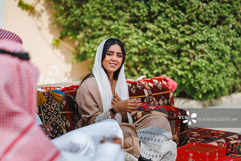 在中东传统户外جلس区，一位中东女性正与朋友一同享用咖啡图片素材