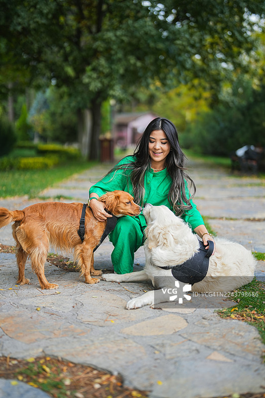 年轻女子身穿绿色服装，在公园里与两只友好的狗狗共度户外时光图片素材