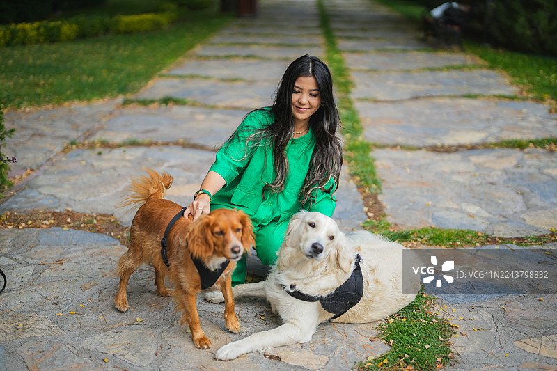 身穿绿色服装的年轻女子在公园里与两条友好的狗狗共度户外时光图片素材