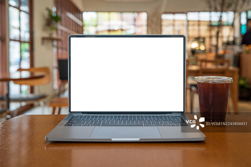 咖啡馆背景下桌上的空白屏幕笔记本电脑。带有复制空间的笔记本电脑屏幕。舒适的工作场所。正面视图。网络冲浪。视频会议。在线购物。图片素材