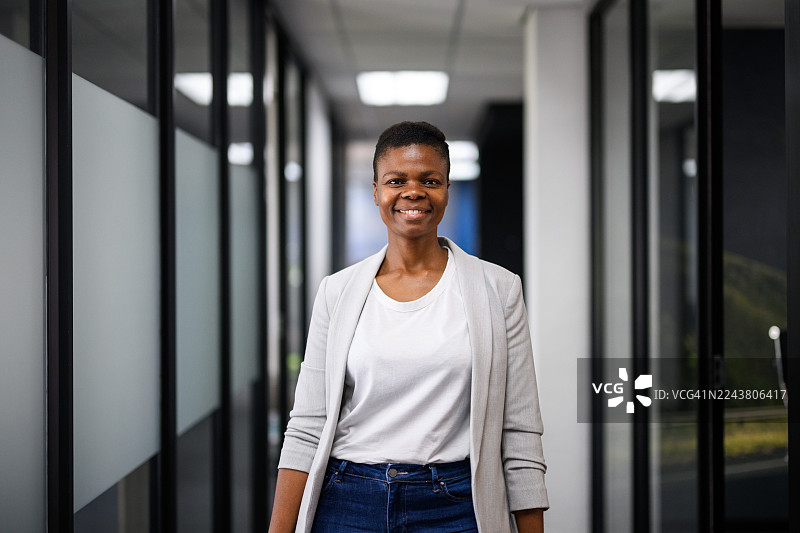 自信的职业女性肖像，在现代办公室走廊里，面带微笑看向镜头图片素材