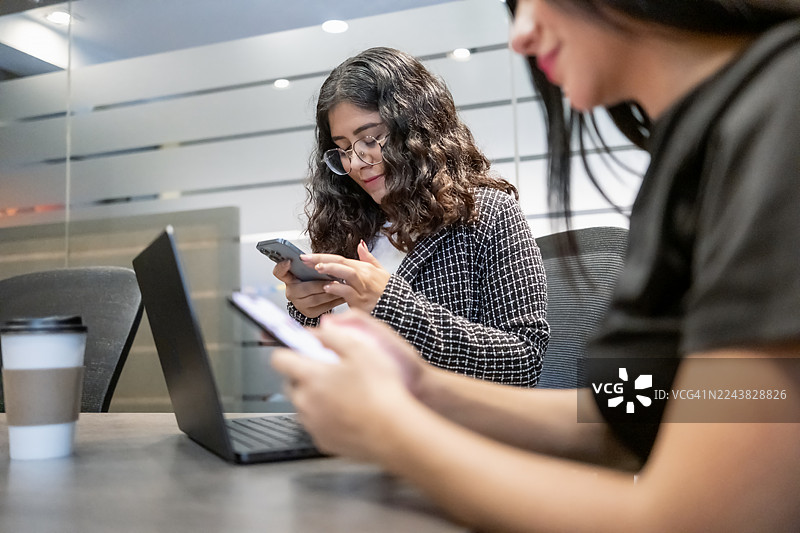 年轻的女高管们在现代化的办公室环境中，愉快而勤奋地使用笔记本电脑和手机工作。图片素材