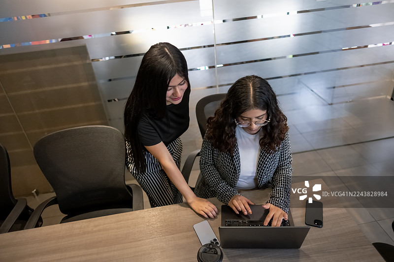 年轻的女高管们在现代化的办公室环境中，快乐勤奋地使用笔记本电脑和手机工作图片素材