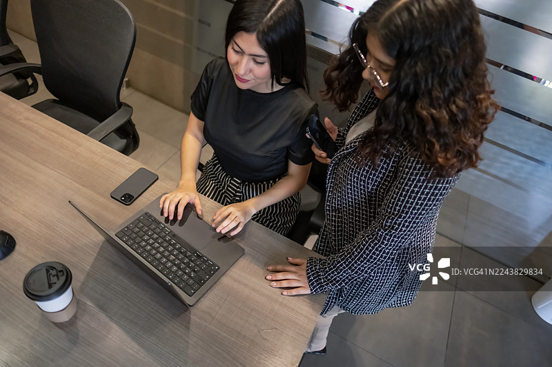 年轻的女高管们在现代化的办公环境中，愉快而勤奋地使用笔记本电脑和手机工作。图片素材