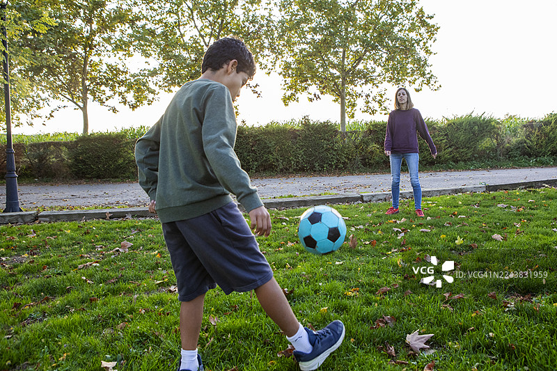 母亲和儿子在日落时分于公园一起踢足球图片素材