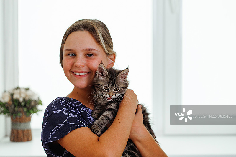 微笑的女孩在室内抱着毛茸茸的小猫，展现出喜悦、温暖和家庭陪伴的温馨画面图片素材