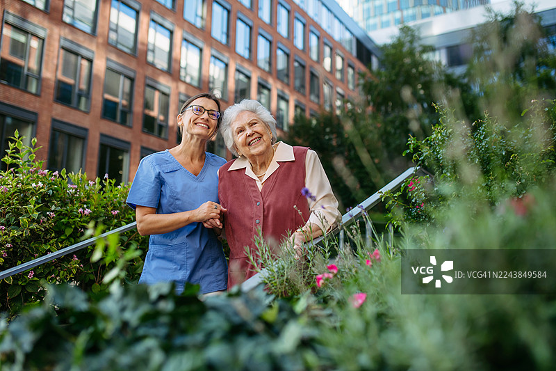 医护人员陪同老年女性在城市公园散步。图片素材
