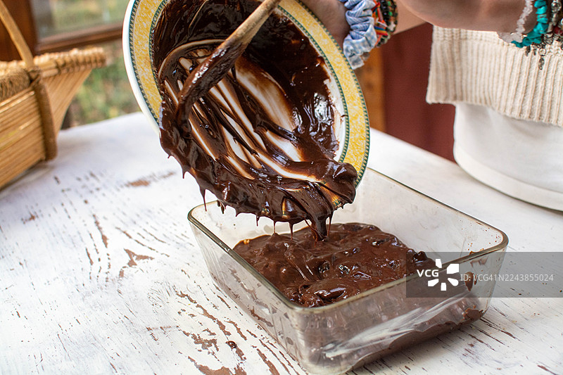 一个人将巧克力布朗尼面糊倒入烤盘图片素材