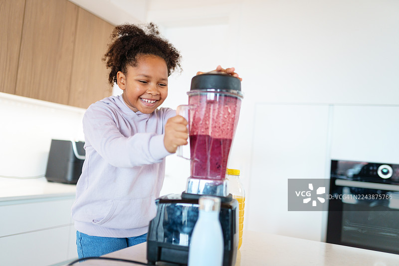 明亮现代厨房里，一位微笑的女孩正在制作浆果冰沙图片素材