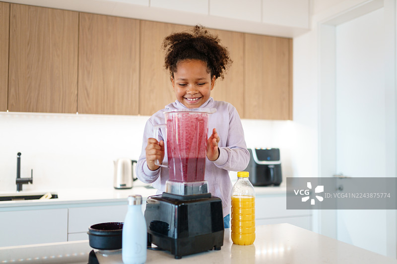 明亮现代厨房里一位微笑着的女孩正在制作冰沙图片素材
