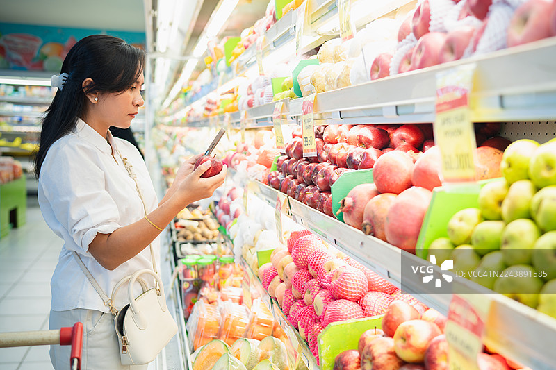 女性在超市挑选水果并使用手机图片素材