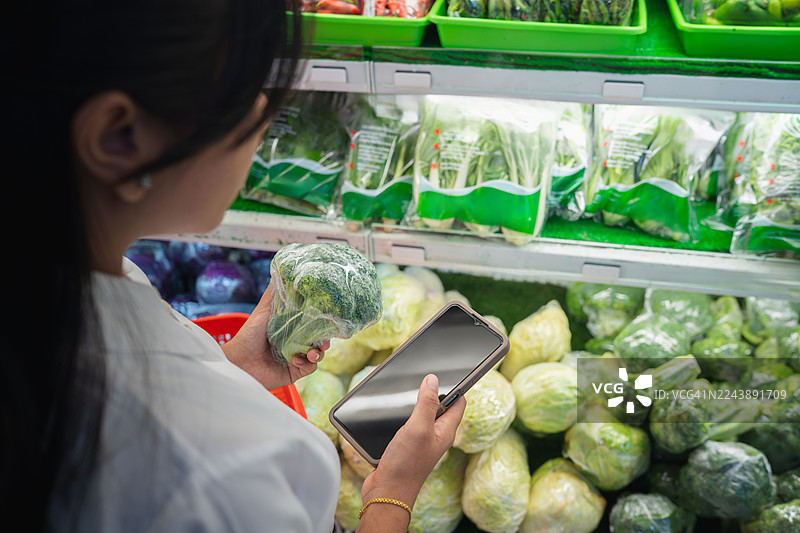 女子在挑选蔬菜时使用智能手机图片素材
