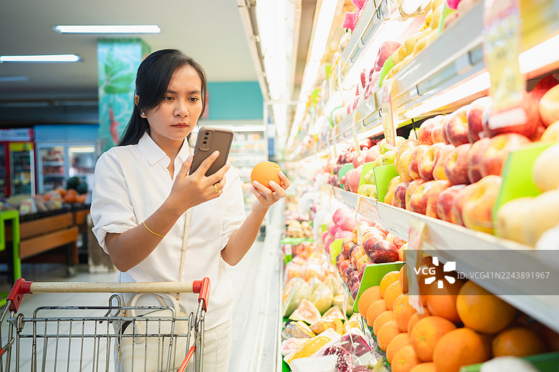 一位女士在超市用智能手机查看水果信息图片素材