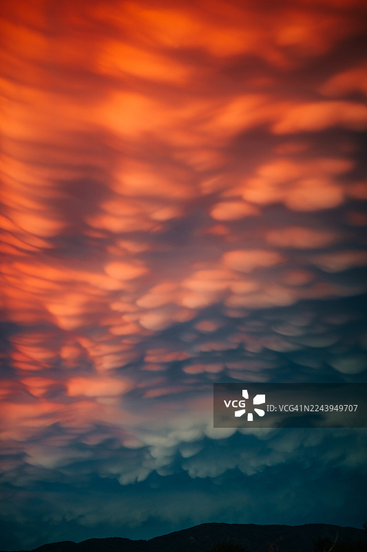 日落或日出时，如火如荼的哺乳状云层特写占据了天空，被鲜艳的红色、橙色和深灰色照亮。图片素材