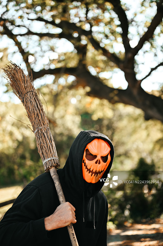 一个人戴着万圣节南瓜面具，在户外拿着扫帚图片素材
