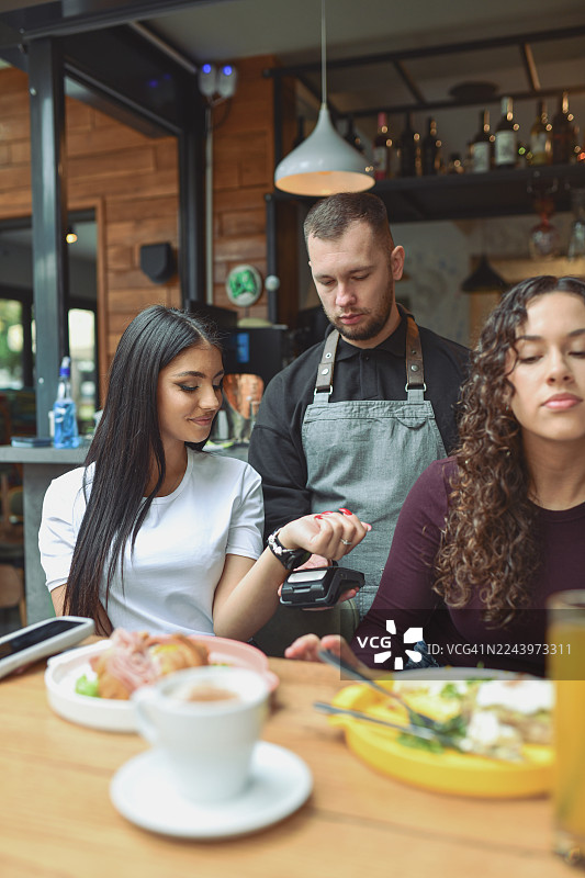 朋友们在现代酒廊酒吧享用早餐，其中一人用手表付款图片素材