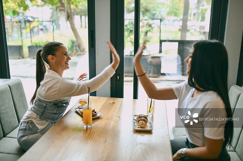 朋友们在明亮现代的咖啡馆里享用早餐，互相击掌，脸上洋溢着笑容图片素材