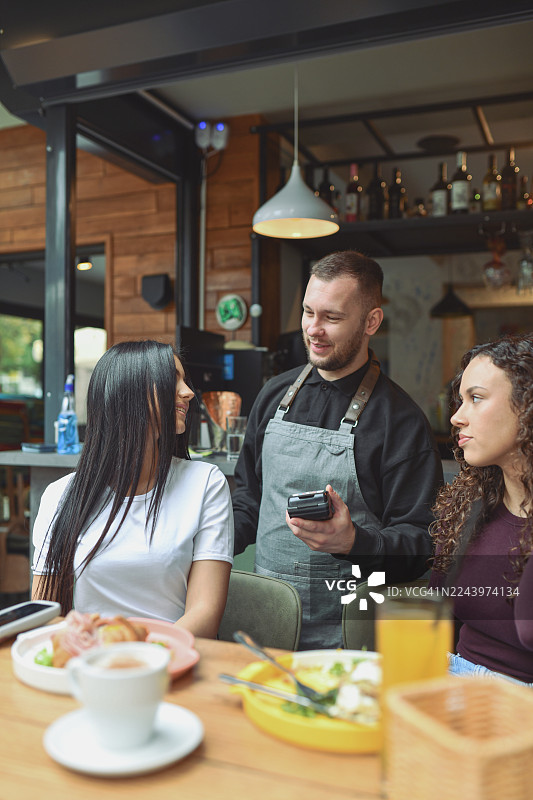 一群朋友在现代休息室酒吧一起享用早餐，一位友好的服务员在旁图片素材