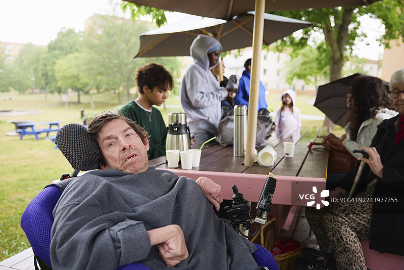 一位患有脑瘫的成熟男子坐在轮椅上，与朋友们在公园里相聚图片素材