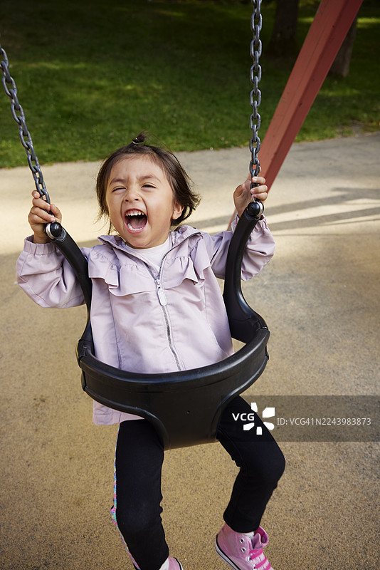 快乐的女孩在公园荡秋千时大声尖叫图片素材