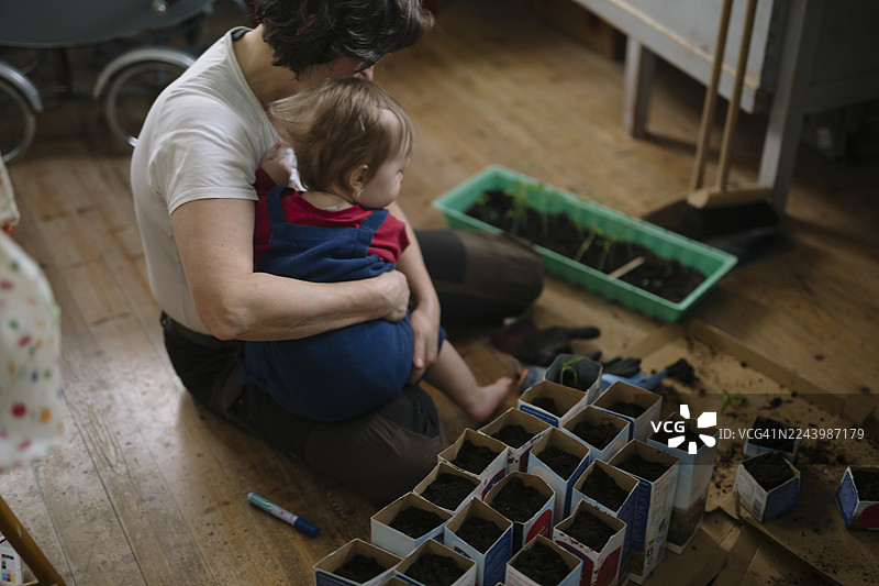 儿子坐在妈妈的腿上，在家做园艺图片素材