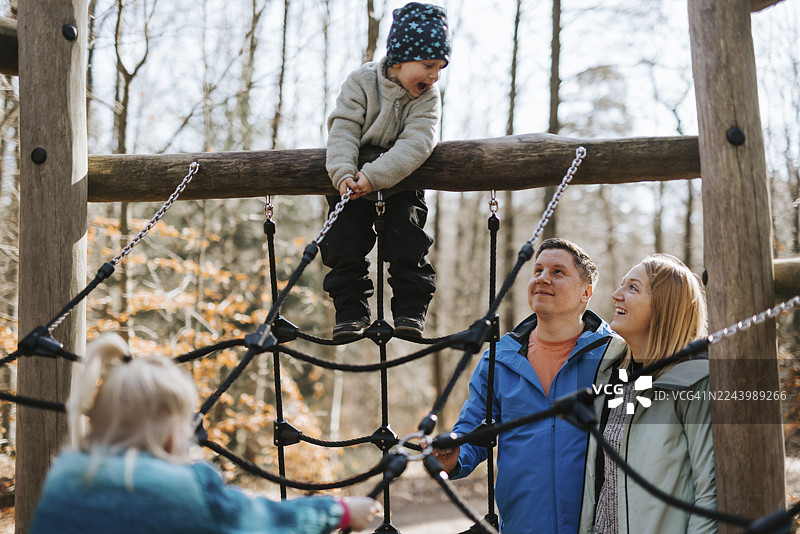 快乐的父母看着儿子在丛林健身架上爬绳图片素材