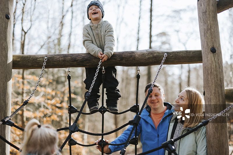 低角度拍摄，一个快乐的小男孩和家人在丛林健身器上玩耍图片素材