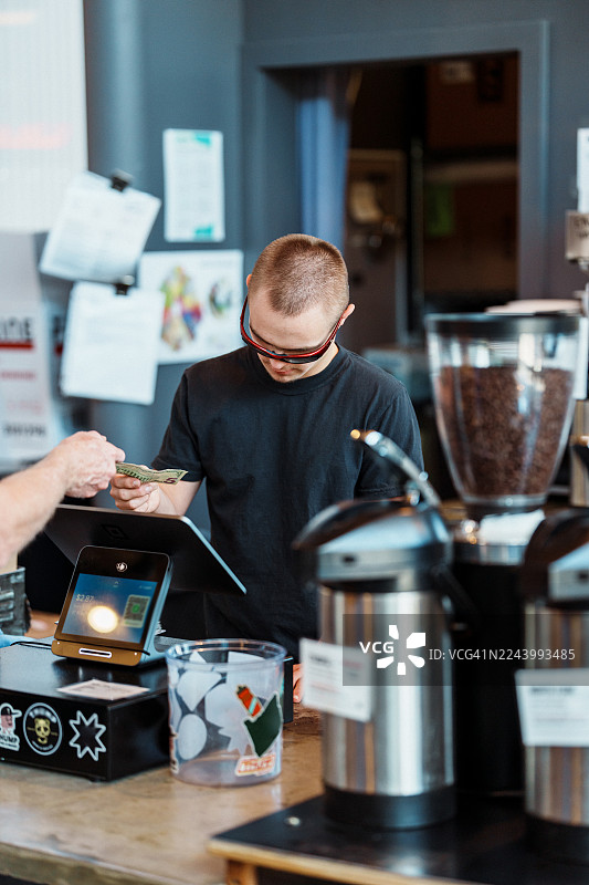 咖啡店里，年轻的咖啡师在收银台工作图片素材