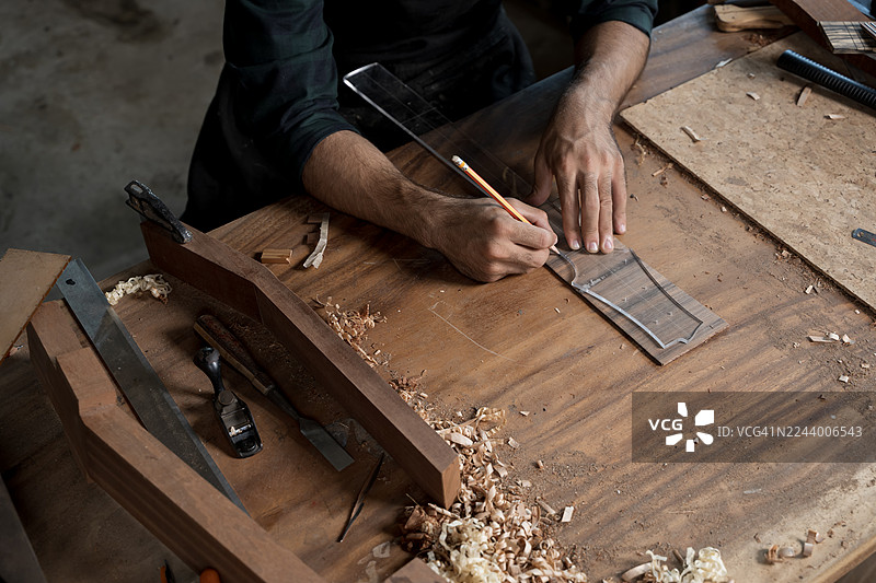 木匠在木工车间的工作台上，使用工具在木板上进行测量和绘制图片素材