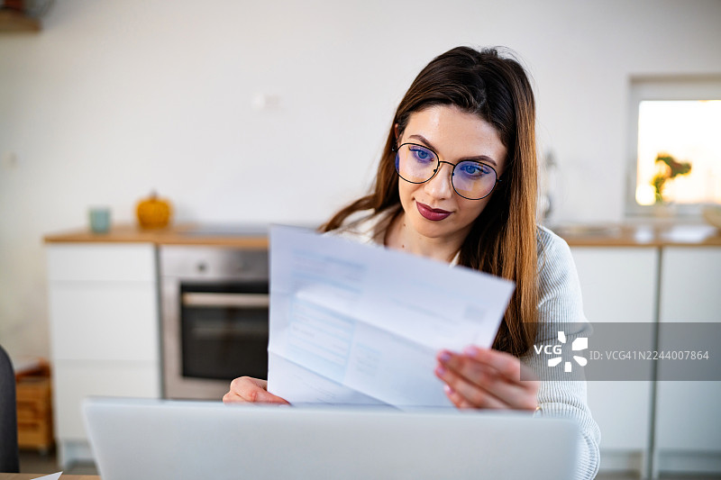 近距离拍摄一名年轻女子戴着眼镜，在家中的笔记本电脑前分析财务报表图片素材