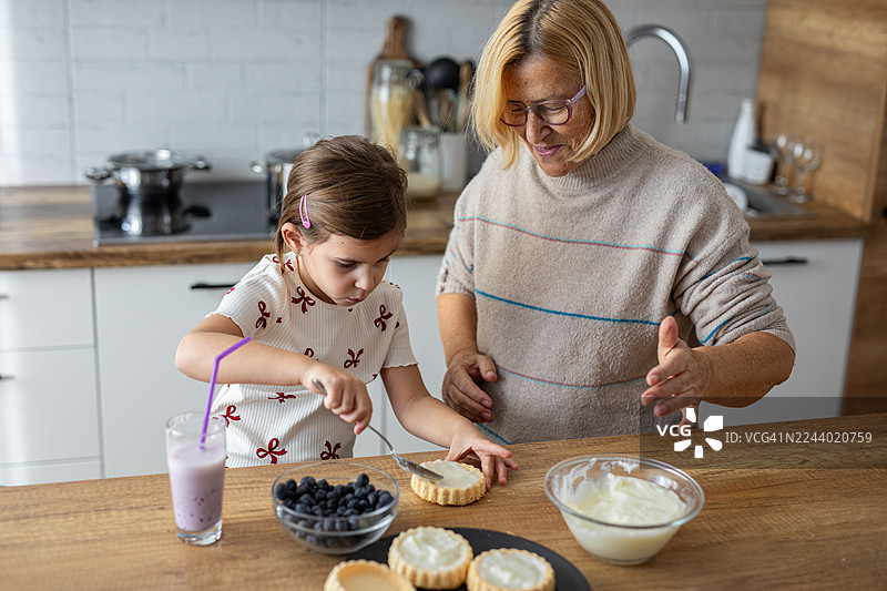 祖母和孙女在温馨的厨房里一起烘焙蓝莓挞图片素材