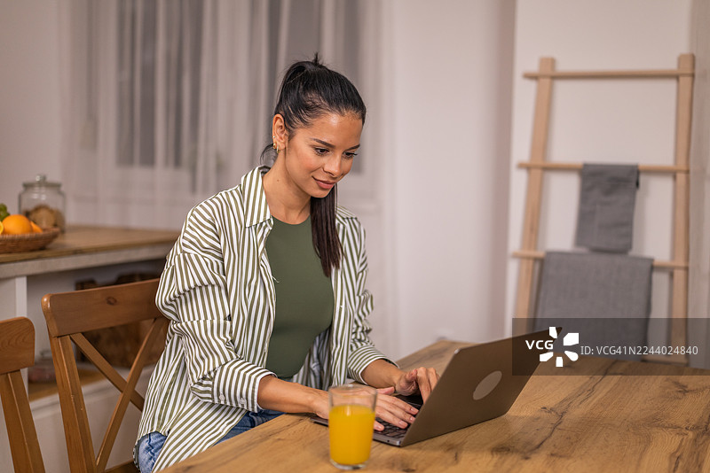 年轻女子在家中自由职业，在现代餐厅中使用笔记本电脑工作。图片素材