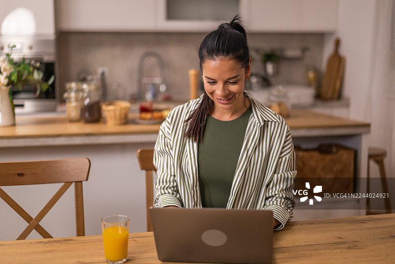 年轻女子在家中自由职业，在现代餐厅里用笔记本电脑工作。图片素材