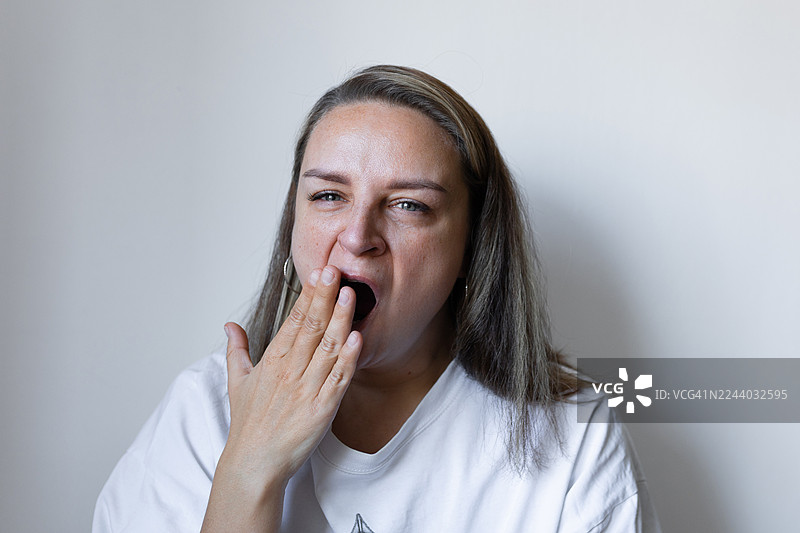 穿着白衬衫打哈欠的女人，在随意的肖像照中流露出疲惫和早晨的困倦图片素材