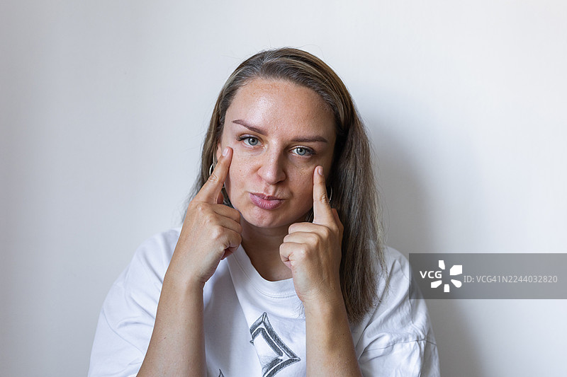 在简约的白色背景下，一位女子在休闲的工作室肖像照中若有所思地触摸着她的太阳穴。图片素材