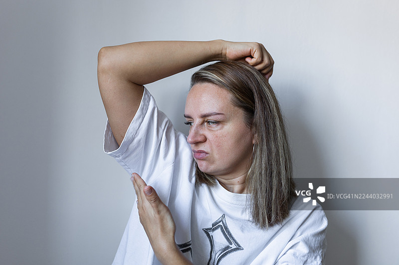 一位女性在随手拍摄的肖像中检查腋下气味，她闻着自己的腋下以判断是否有汗味。图片素材