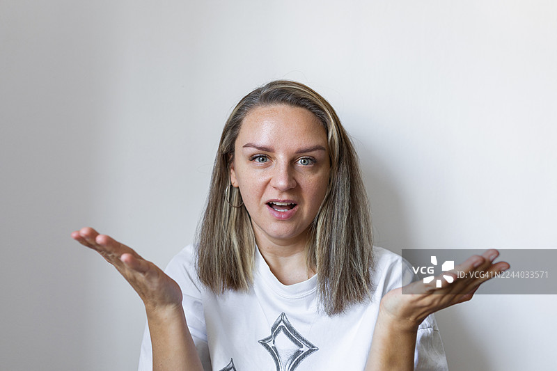 一位女性的面部肖像，表情带着疑问，双手张开，身穿休闲白色T恤图片素材