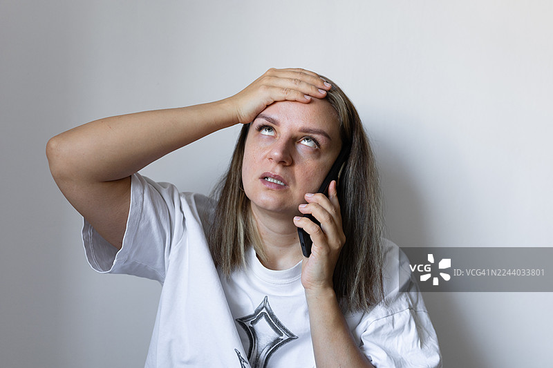 一位女性在室内场景中，边打电话边用手扶着额头，显得十分焦虑图片素材