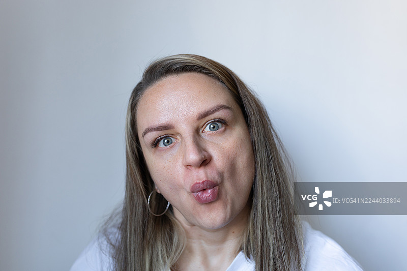 特写镜头，一位女性噘着嘴、眨着明亮的蓝眼睛，做出亲吻的表情图片素材