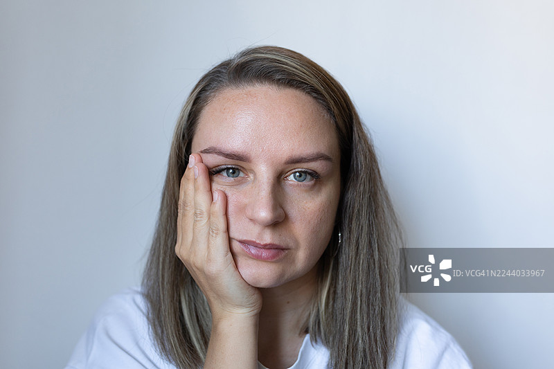 一位疲惫的女子肖像，她用手托着脸颊，若有所思，神情沉郁。图片素材