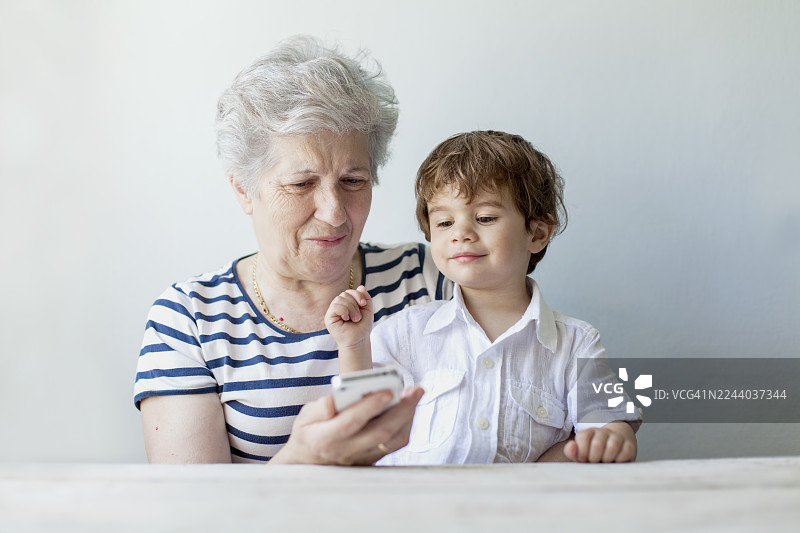 祖母和孙子在明亮的房间里一起探索智能手机，共享欢乐时光图片素材