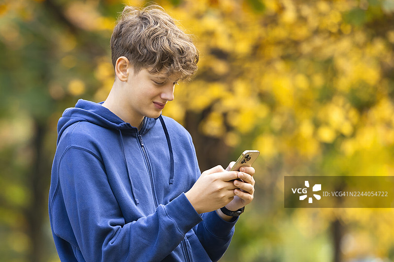 秋季校园公园里，一名十几岁的学生正在使用智能手机图片素材