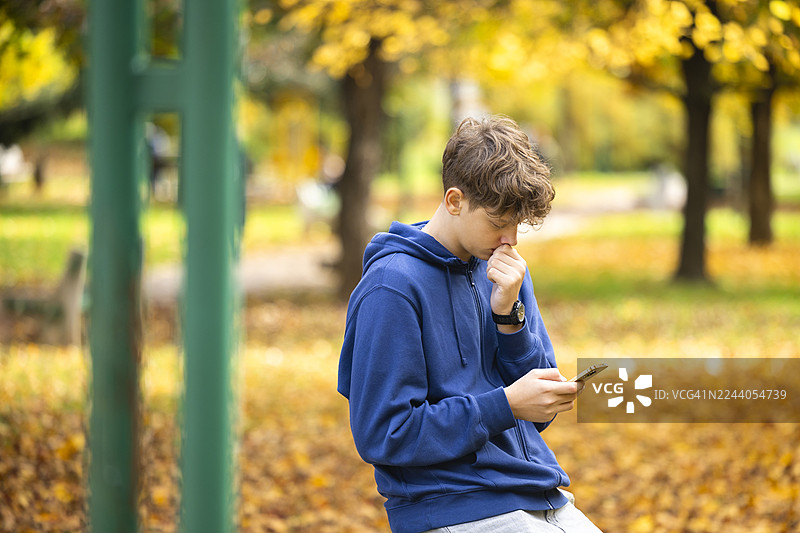 秋季校园公园里，一名十几岁的学生正在玩智能手机。图片素材