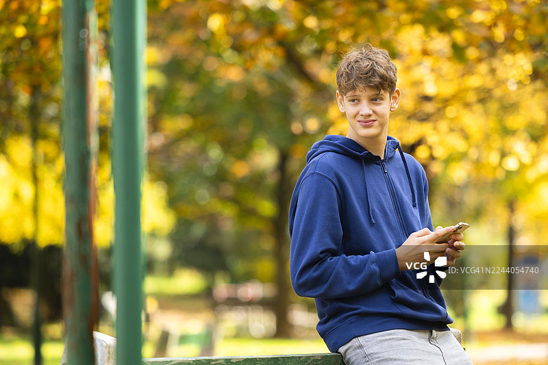 秋季校园公园里，一名十几岁的学生正在玩手机图片素材