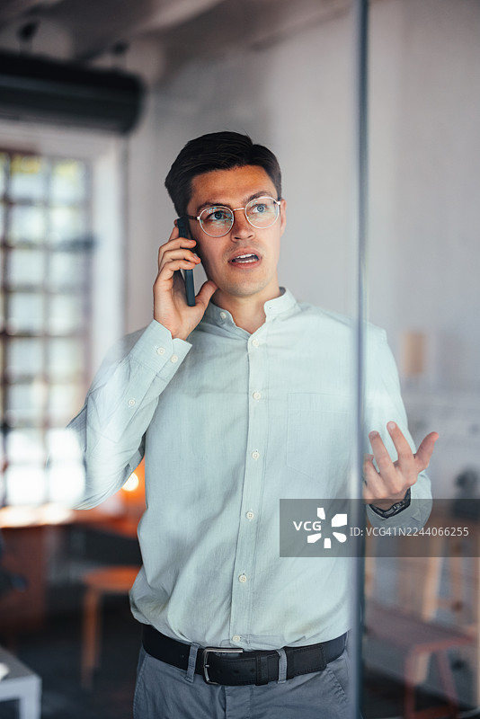 现代办公室里，一位专业男士正在打电话，在玻璃墙后讨论业务图片素材