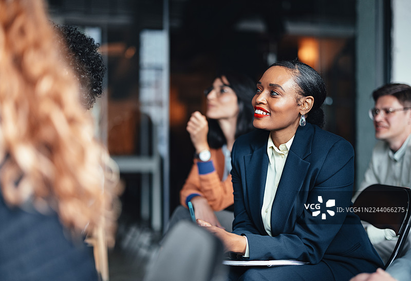 职业化小组会议，一位身穿海军蓝西装的女士在办公室讨论中面带微笑图片素材