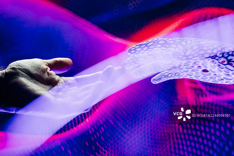 一只人类的手轻轻地伸向一只白色的、未来感十足的机械手，周围环绕着旋转的抽象光线和充满活力的品红色与蓝色的数字图案。图片素材