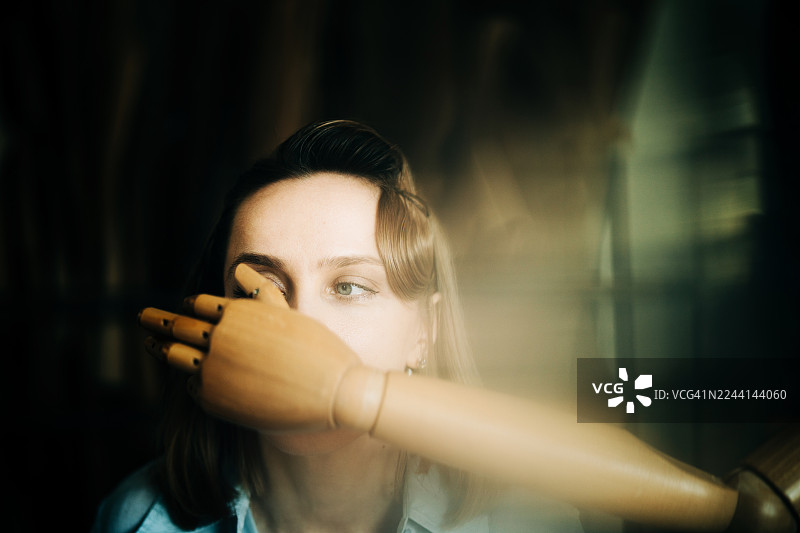 前景中，一只木制人体模型的手捂住了女人的嘴，这是一张特写肖像照。主题涉及沉默、审查和身份模糊。图片素材