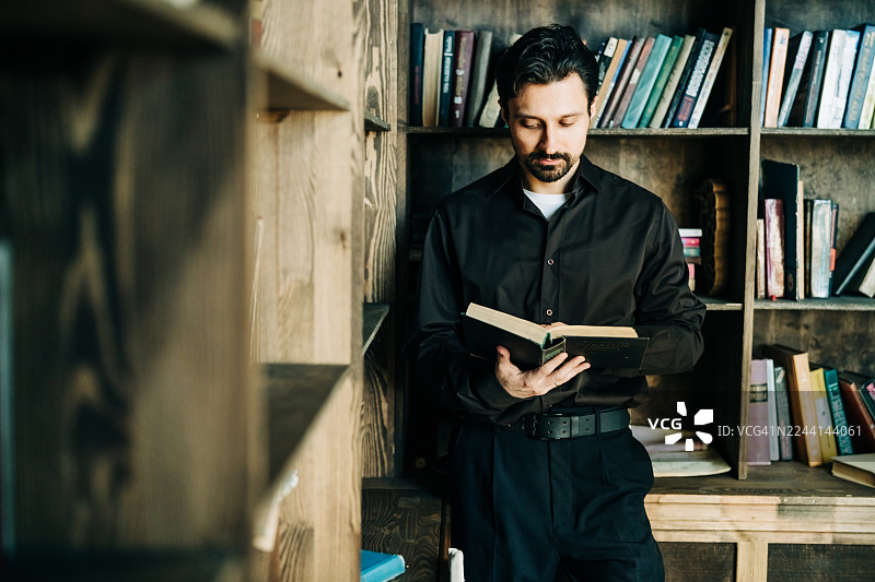 一位衣着考究、神情专注的男士站在图书馆里，沉浸于书本之中。这幅严肃的肖像传达出求知探索、经典风格以及对知识的渴望。图片素材