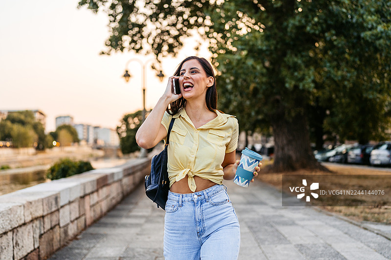 年轻女子在码头边边走边打电话和喝外带咖啡图片素材